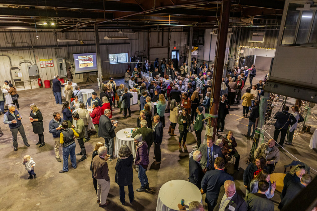 A large group of people enjoying a party inside a large garage space|Two rows of annual report booklets|A series of framed documents and awards.|Group of eight people standing and smiling at the camera